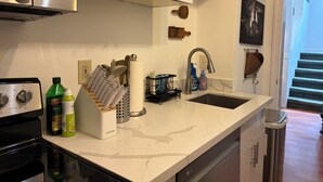 Une cuisine moderne dotée d’une cuisinière en acier inoxydable, d’un four encastré, d’un évier à deux bacs et d’un plan de travail sur lequel sont disposés divers ustensiles et appareils de cuisine.