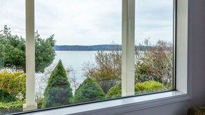 Une vue depuis une fenêtre donnant sur un lac, avec des arbres et une rive éloignée.