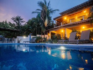 Relax by the serene pool surrounded by lush tropical vegetation and lounge chairs.