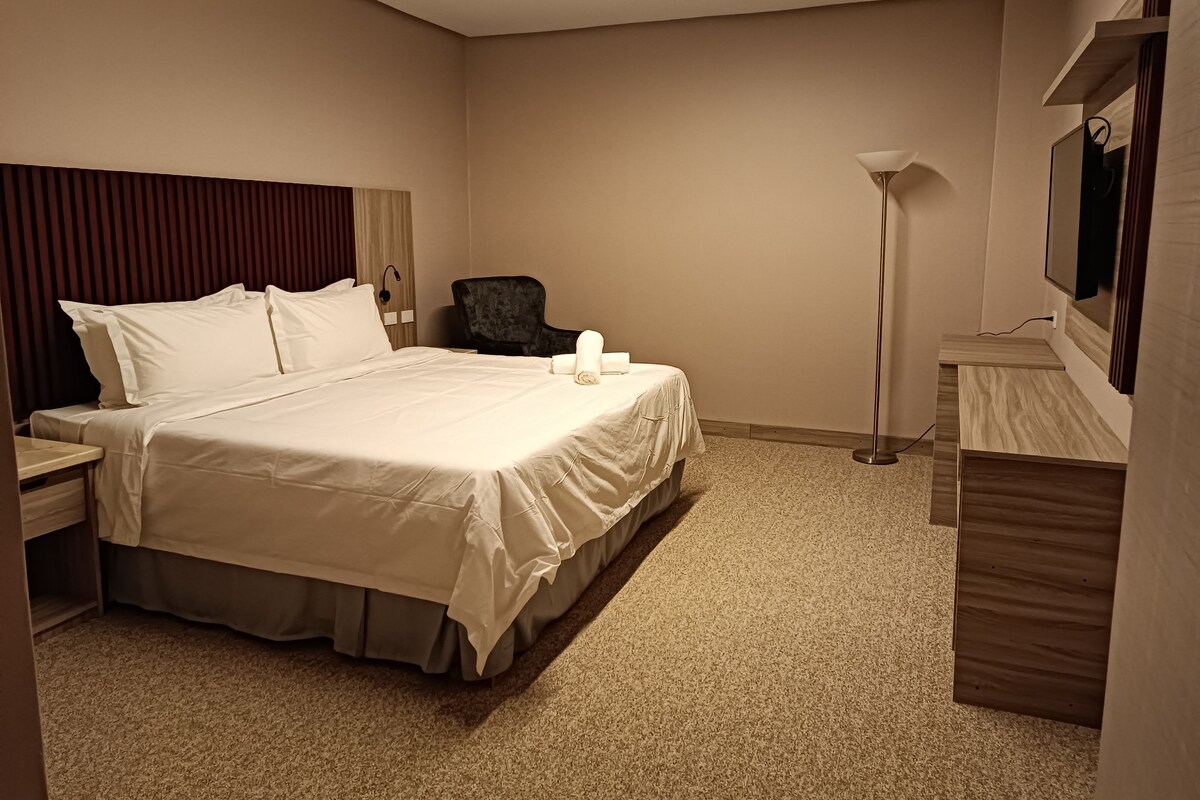 Een hotelkamer met een groot bed, een bureau, een stoel, een lamp en een spiegel.