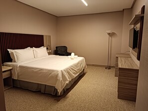A hotel room with a large bed, a desk, a chair, a lamp, and a mirror.