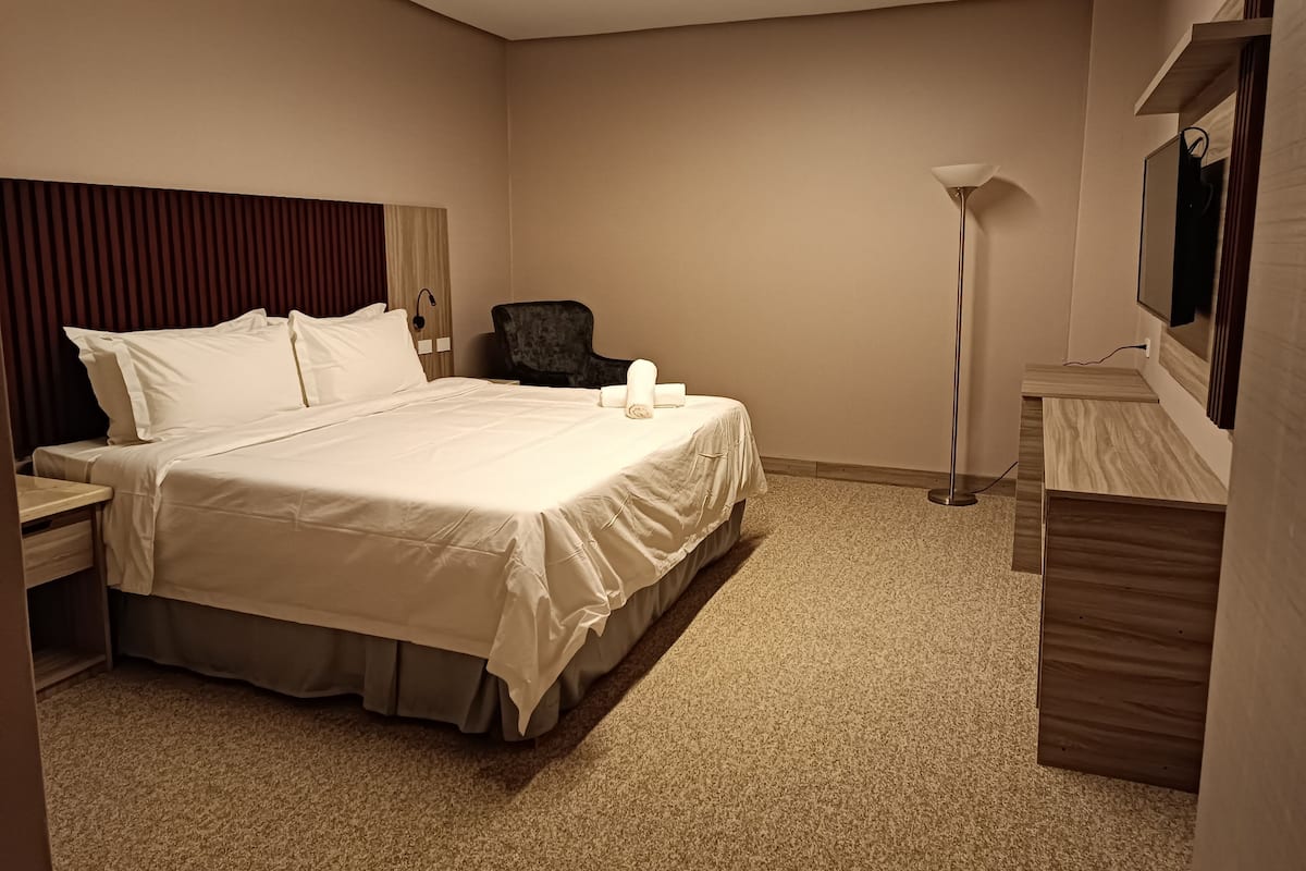 A hotel room with a large bed, a desk, a chair, a lamp, and a mirror.