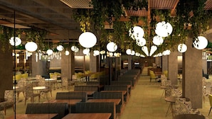 Un amplio comedor interior con varias mesas y sillas, lámparas esféricas colgantes y plantas.