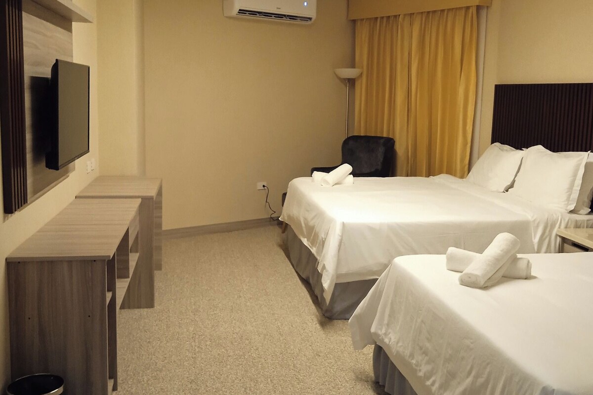 Een hotelkamer met twee bedden, een bureau, een stoel, een airconditioner en een televisie.