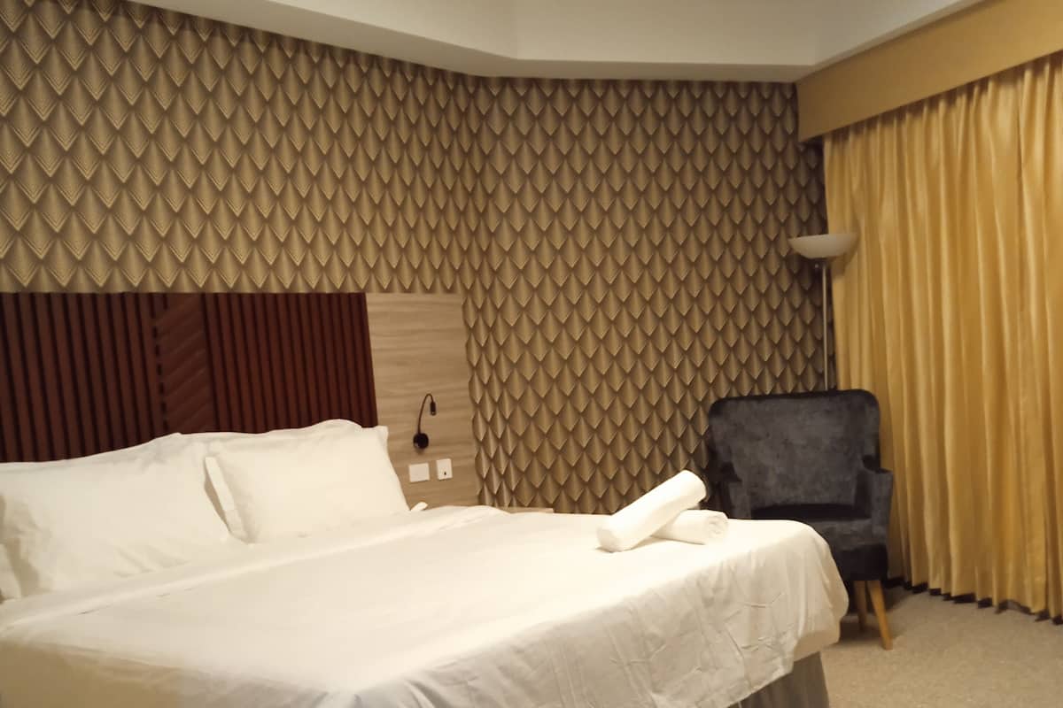 A hotel room with a large bed, a chair, and a patterned wall.