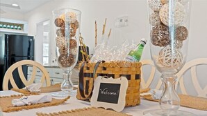 A dining table set with clear glassware, a wicker basket with a 'Welcome!' sign, and a bottle of champagne. - Coastal Chic House in Cocoa Beach w/Private Yard - Walk to Beach, Pier & Ron-Jon (Cocoa Beach)