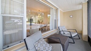 A room with a large sliding glass door leading to a dining area, two wicker chairs with cushions, a clock on the wall, and a ceiling with wooden paneling. - Coastal Chic House in Cocoa Beach w/Private Yard - Walk to Beach, Pier & Ron-Jon (Cocoa Beach)