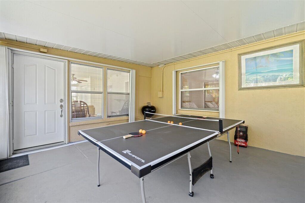 Une table de ping-pong dans une pièce dotée d’une porte, de fenêtres et d’un tableau accroché au mur.