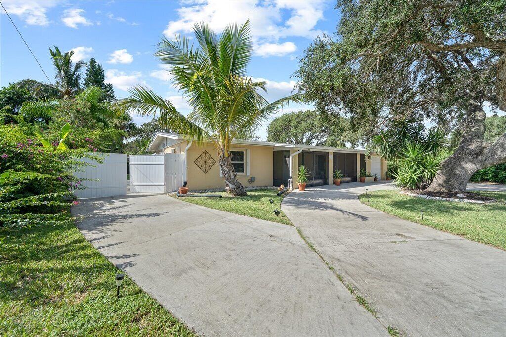 A single-story house with a front yard, a palm tree, and a large tree to the right.