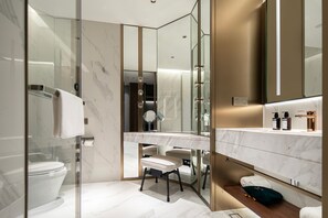 Een moderne badkamer met een douchecabine van glas, een toilet, een wastafel met spiegel en een bankje.