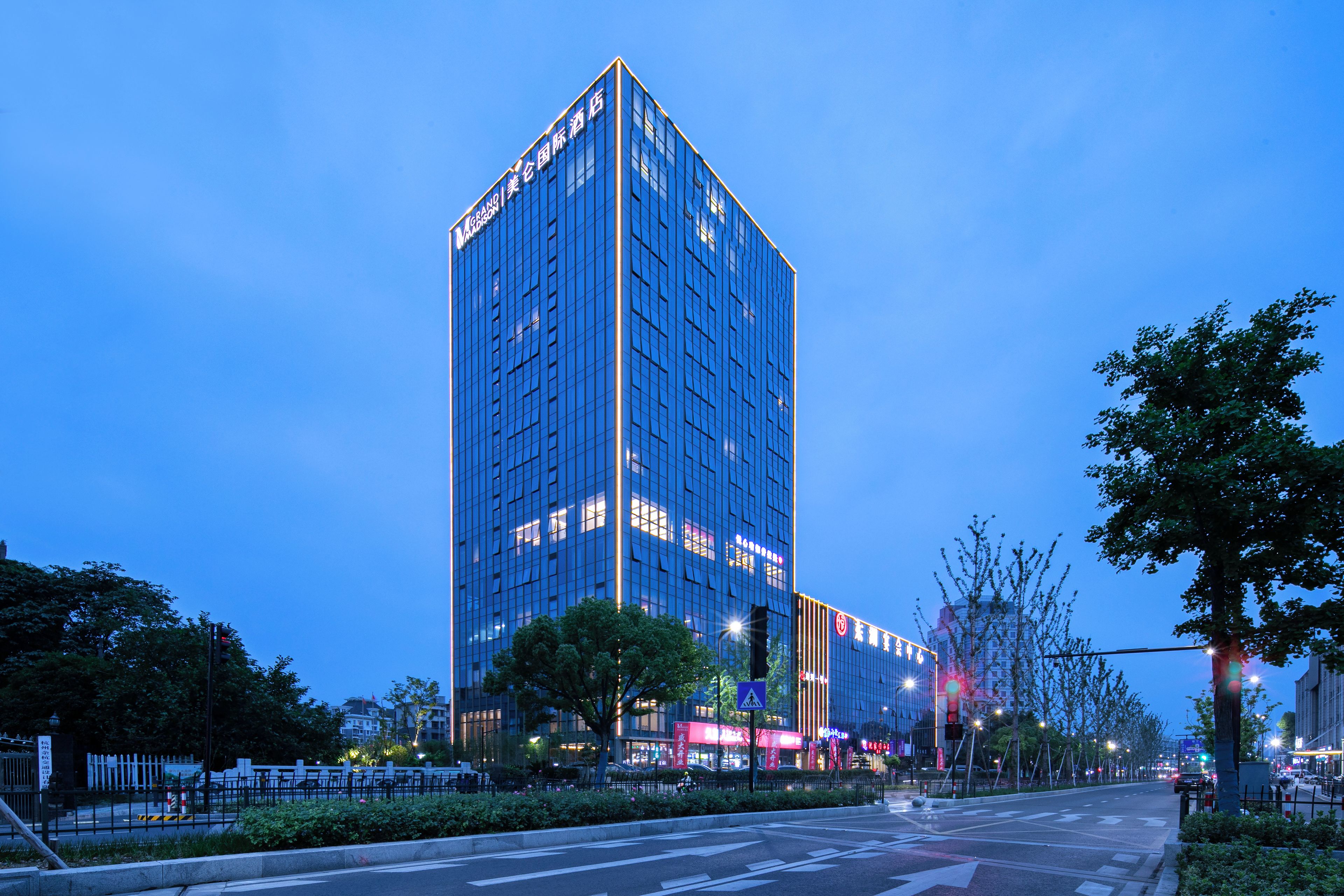 A high-rise hotel with a modern glass facade, located at a city intersection with street lights and trees.