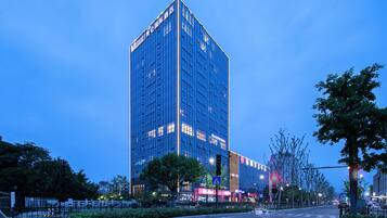 A high-rise hotel with a modern glass facade, located at a city intersection with street lights and trees.