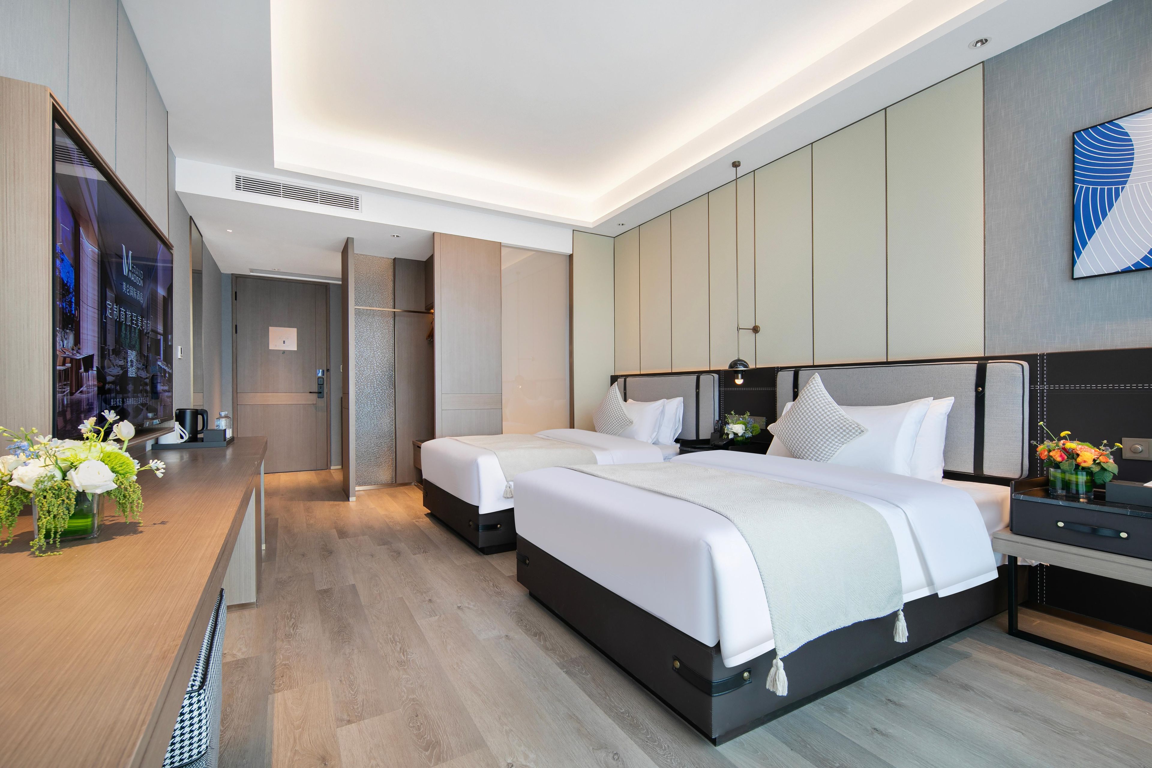 Una habitación de hotel moderna con dos camas, un escritorio de madera con un florero y un ventanal grande.
