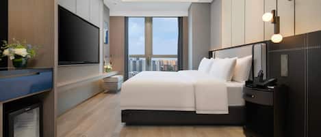 Ein modernes Hotelzimmer mit einem großen Bett, einem Flachbildfernseher, einem Schreibtisch und Blick auf die Stadtlandschaft.