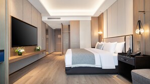 Een moderne hotelkamer met een grote flatscreen televisie, een bed met witte lakens, een nachtkastje met een lamp en een houten vloer.