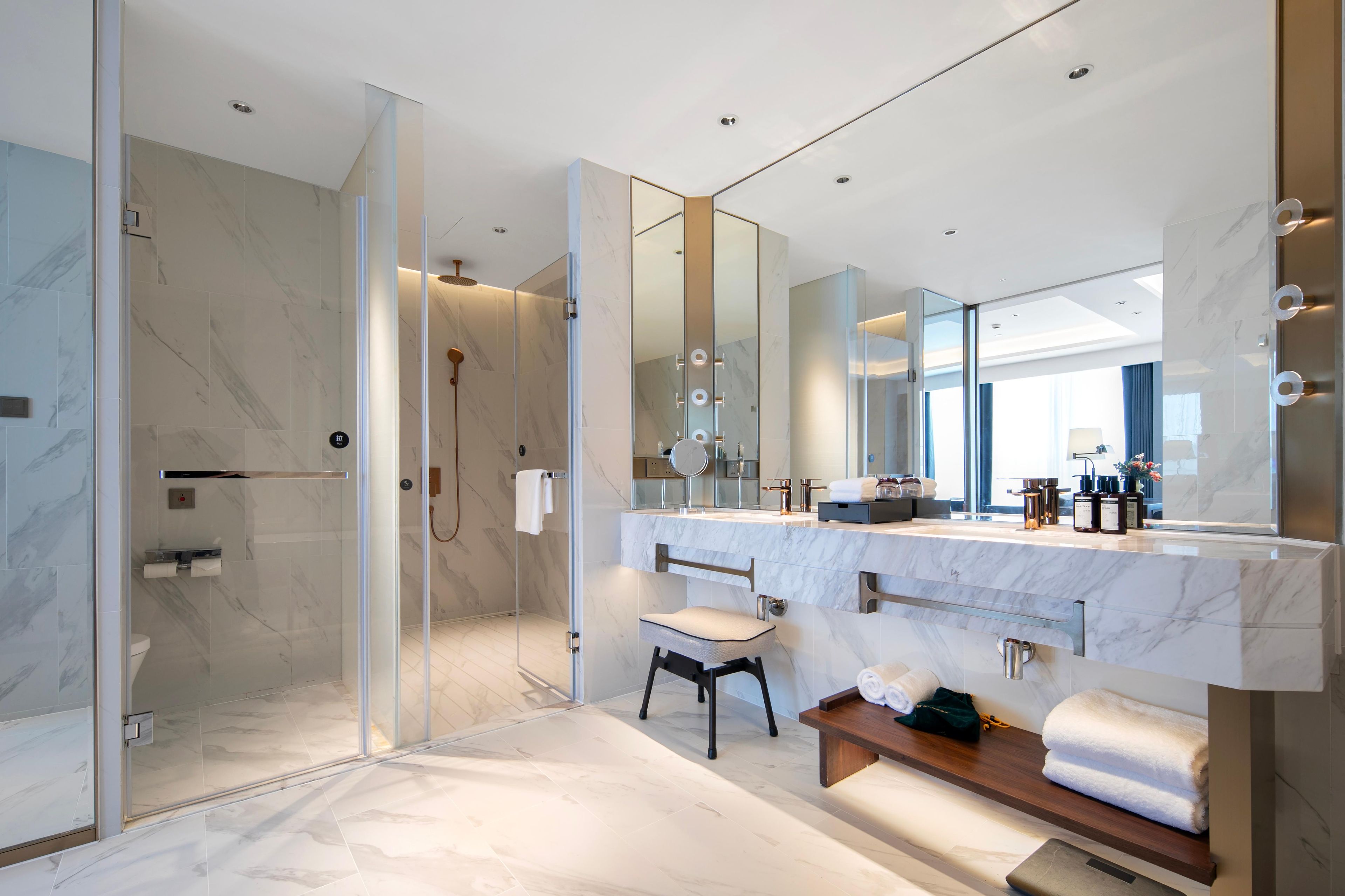 Een moderne badkamer met een douchecabine van glas, een grote spiegel en een wastafel met een marmeren aanrechtblad.