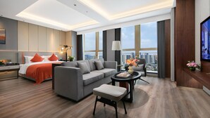 Een moderne hotelkamer met een bed, een grijze bank en een televisie.
