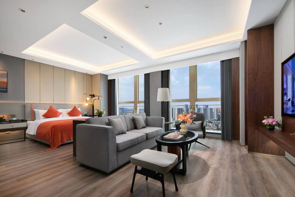 A modern hotel room with a bed, grey sofa, and a TV.