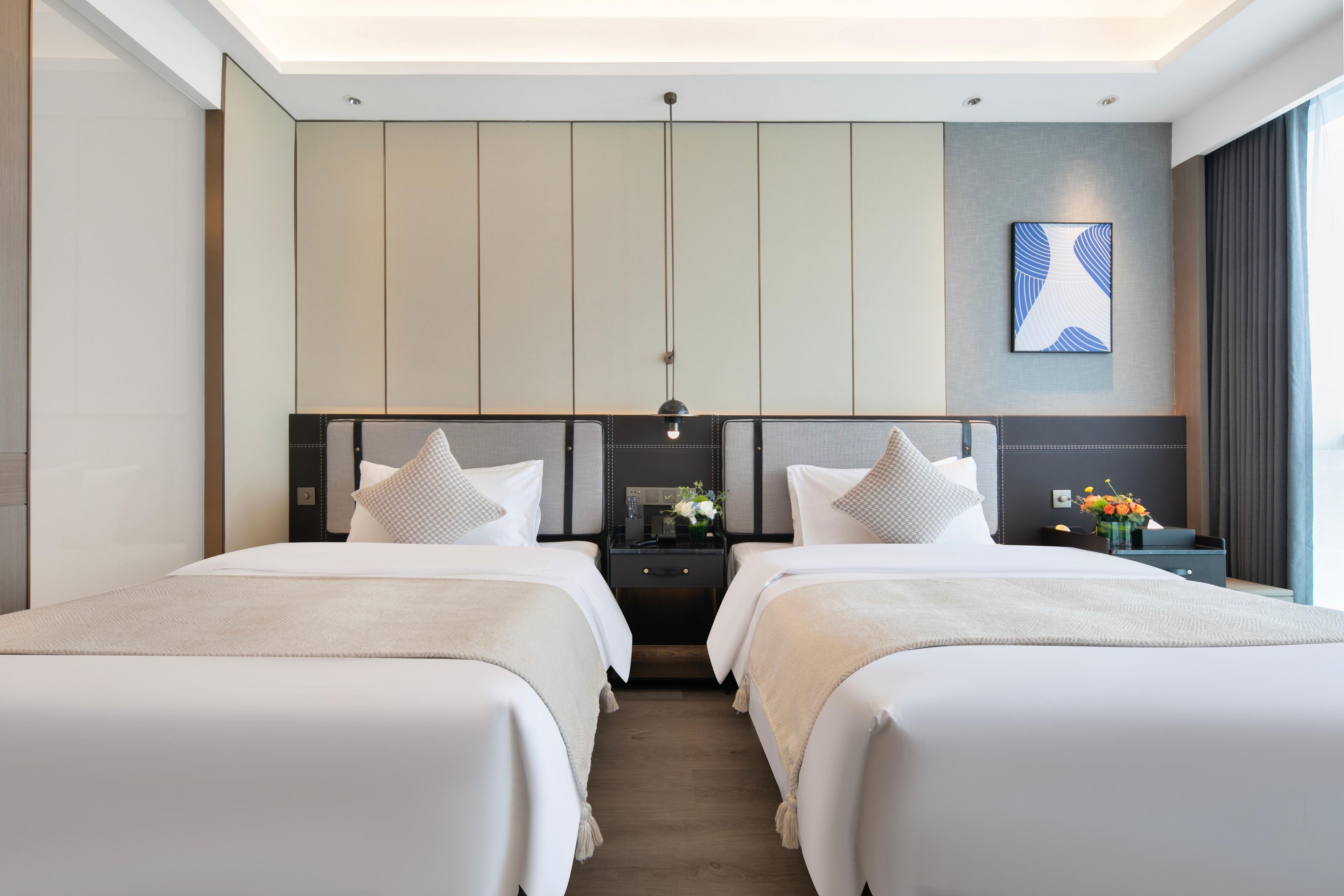 Una habitación de hotel moderna con dos camas, una mesita de noche con lámpara y una obra de arte colgada en la pared.