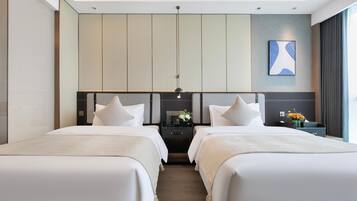 A modern hotel room with two beds, a nightstand with a lamp, and a wall-mounted artwork.