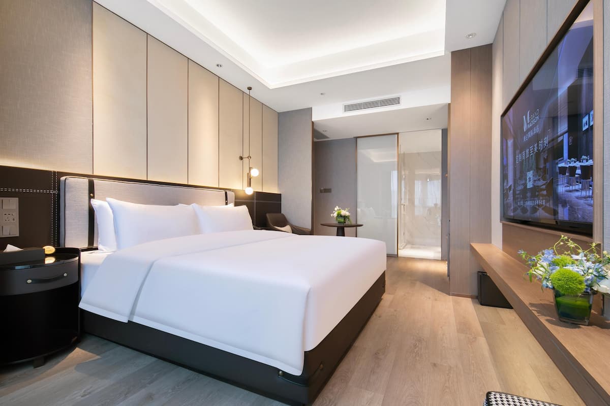 A modern hotel room with a large bed, a TV mounted on the wall, and a small table with a vase of flowers.