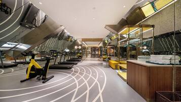 A modern gym with exercise equipment, a reception desk, and a mirror wall.