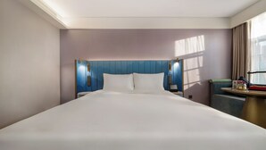 Una habitación de hotel con una cama grande, cabecera con iluminación integrada, mesita de noche y una ventana con cortinas.