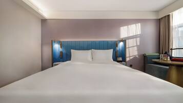 A hotel room with a large bed, a headboard with built-in lighting, a bedside table, and a window with curtains.