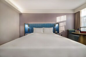 Una habitación de hotel con una cama grande, cabecera con iluminación integrada, mesita de noche y una ventana con cortinas.