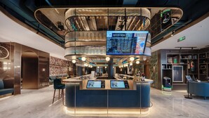 A modern lobby with a central reception desk, a digital information screen, and a staircase leading to an upper level. - Manxin Hotel Hefei Jingkai District Pearl Plaza (Hefei)