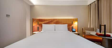 Habitación de hotel con una cama grande, un escritorio con computadora, una silla y una ventana con cortinas.