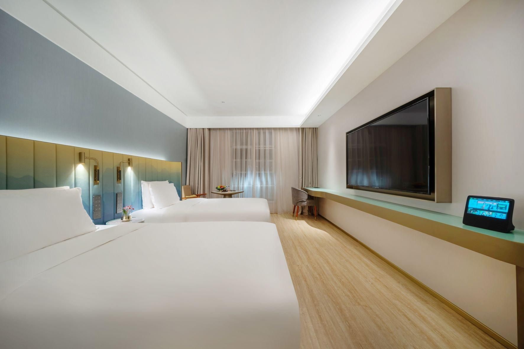 A hotel room with two beds, a TV, a desk, and a digital device on the desk.