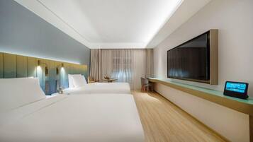 A hotel room with two beds, a TV, a desk, and a digital device on the desk.
