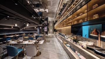 A modern restaurant interior with a long counter, seating area, and decorative lighting.
