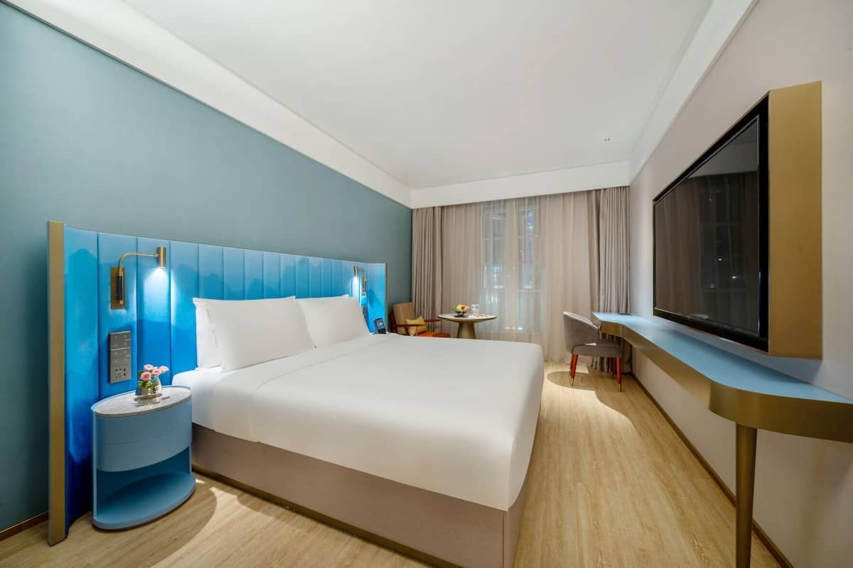 A modern hotel room with a large bed, a desk, a TV, and a small table with a vase of flowers.