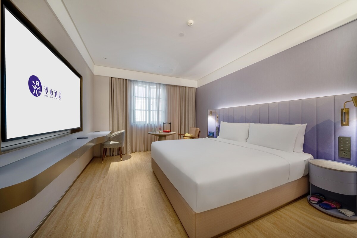 Una habitación de hotel moderna con una cama grande, un escritorio y una pantalla de televisión que muestra un logo.