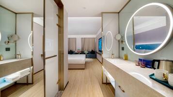 A hotel room with a bed, a sitting area, a bathroom with a mirror, and a TV.