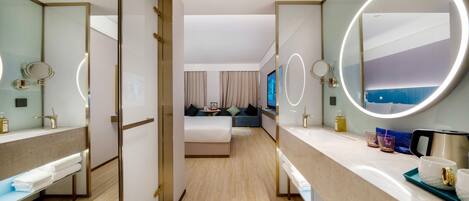 A hotel room with a bed, a sitting area, a bathroom with a mirror, and a TV.