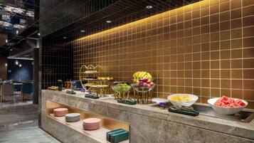 A buffet area with various fruits and bowls of food, a seating area with chairs, and a tiled wall.