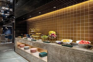 Zona de buffet con diversas frutas y fuentes de comida, un área de estar con sillas y una pared de azulejos.