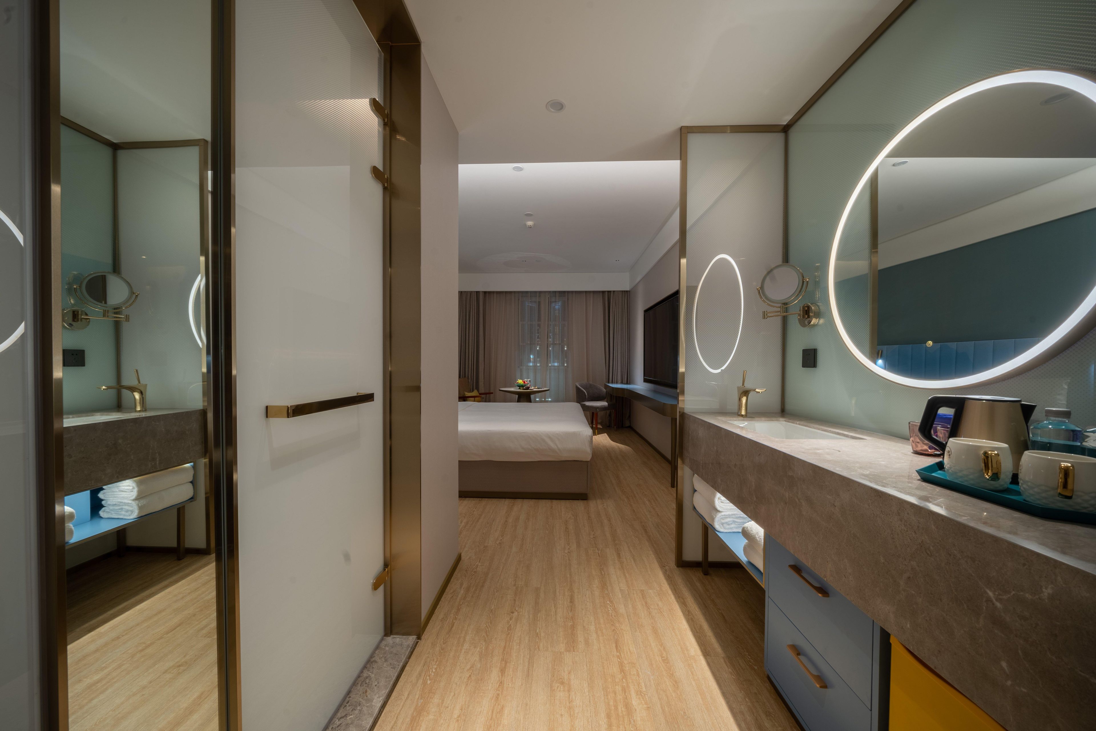 Habitación de hotel con una cama grande, una zona de estar con mesa y sillas, un baño con espejo y lavamanos, y un minibar.