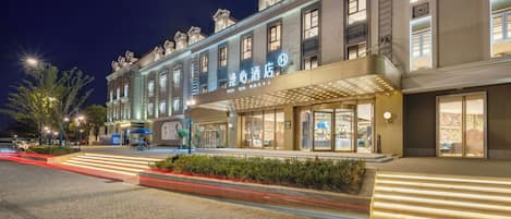 A hotel with a classic European architectural style, featuring a grand entrance with a canopy and illuminated signage.