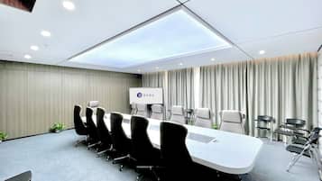 A conference room with a long table, chairs, a projector screen, and curtains.