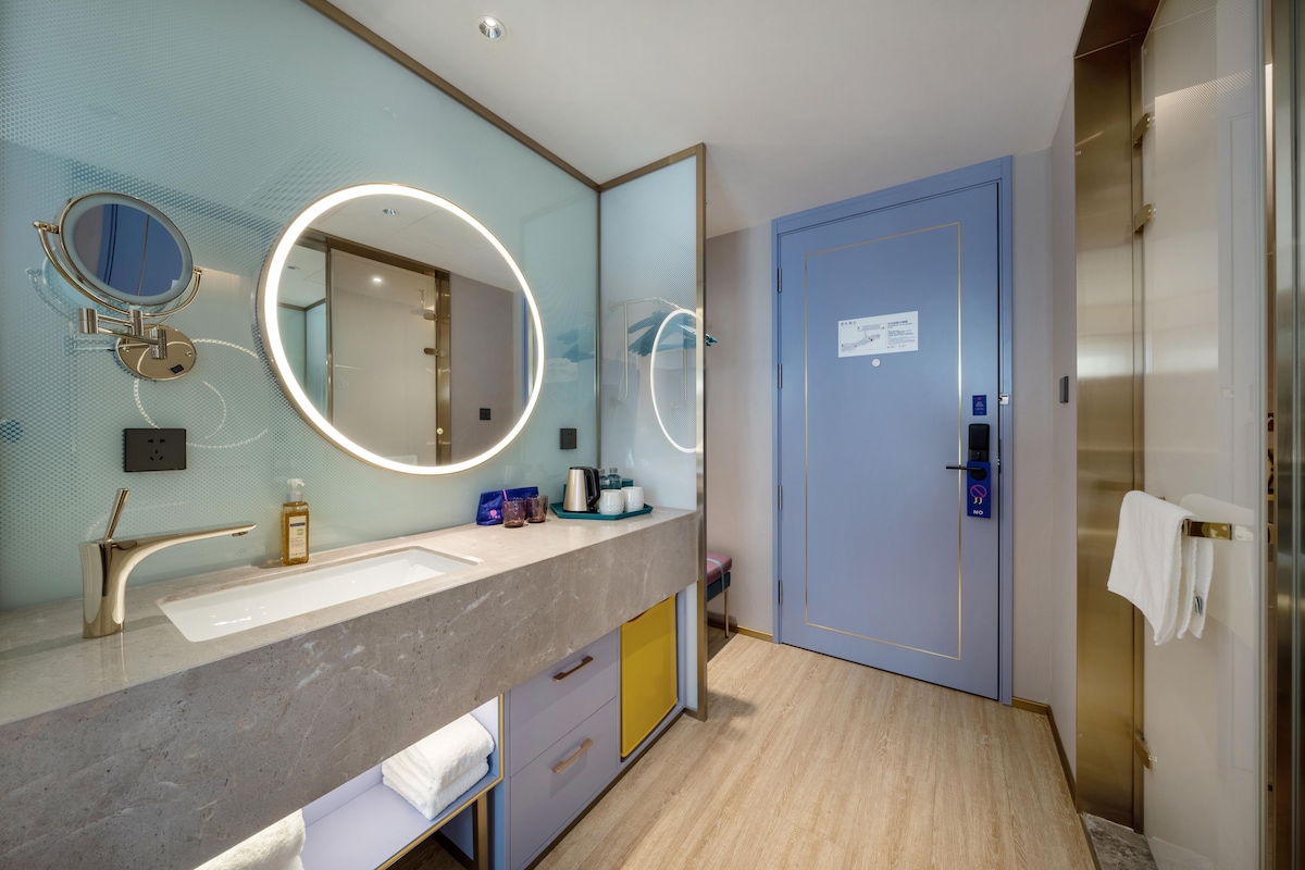 Un baño moderno con tocador de mármol, un espejo grande con luces circulares, un perchero y una puerta con un letrero.