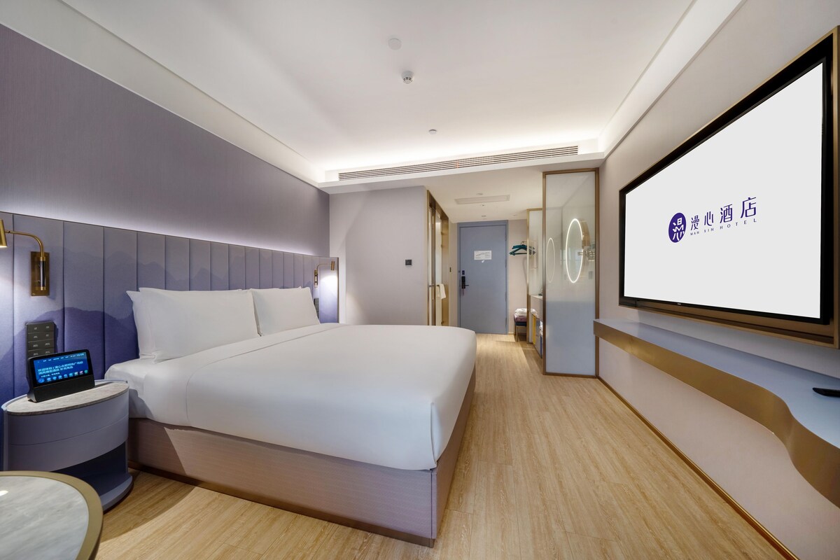 Una habitación de hotel moderna con una cama grande, un panel de control junto a la cama, un televisor de pantalla plana y un mostrador de recepción.