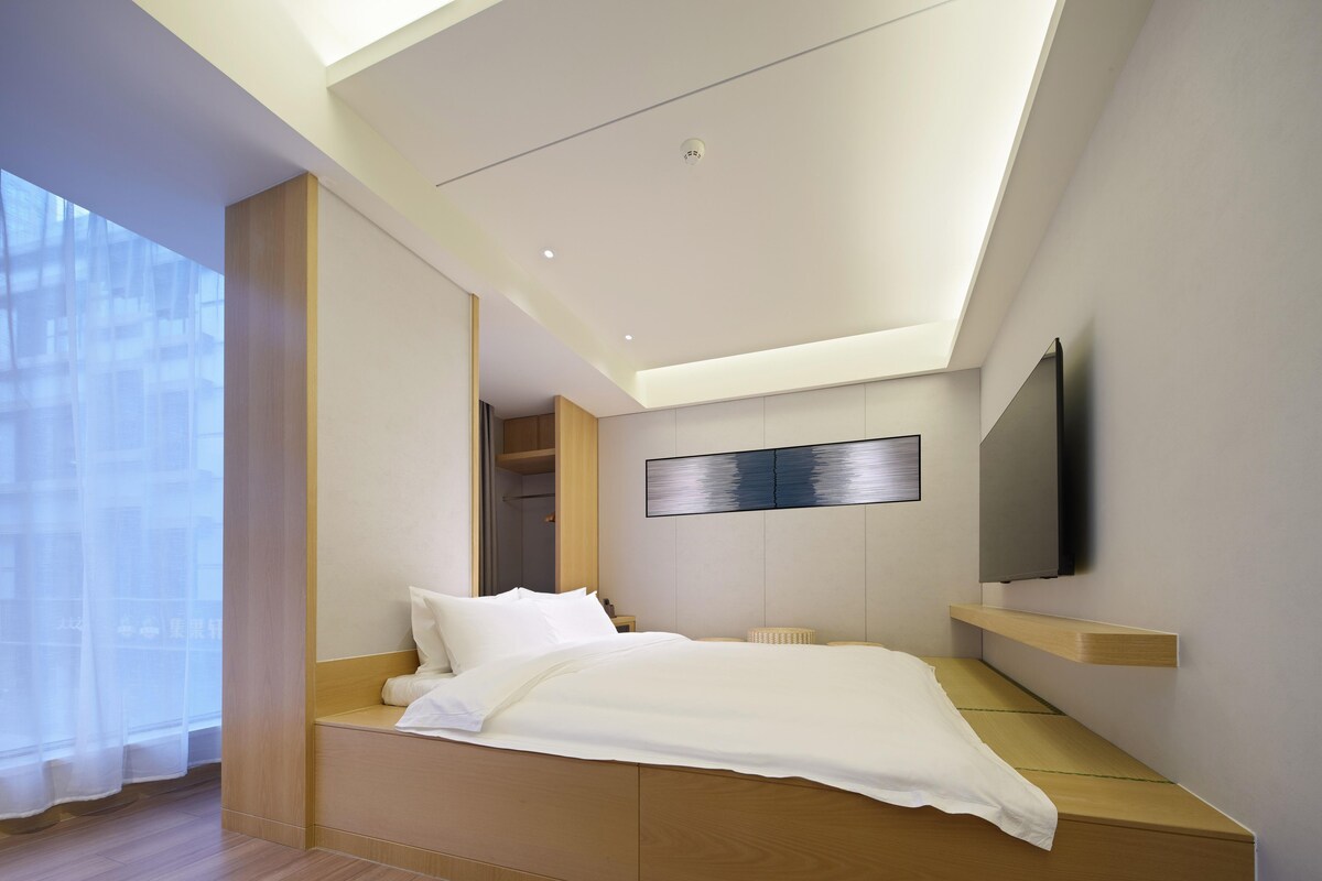 Une chambre à coucher moderne avec un lit, des étagères intégrées, un téléviseur fixé au mur et une grande fenêtre.