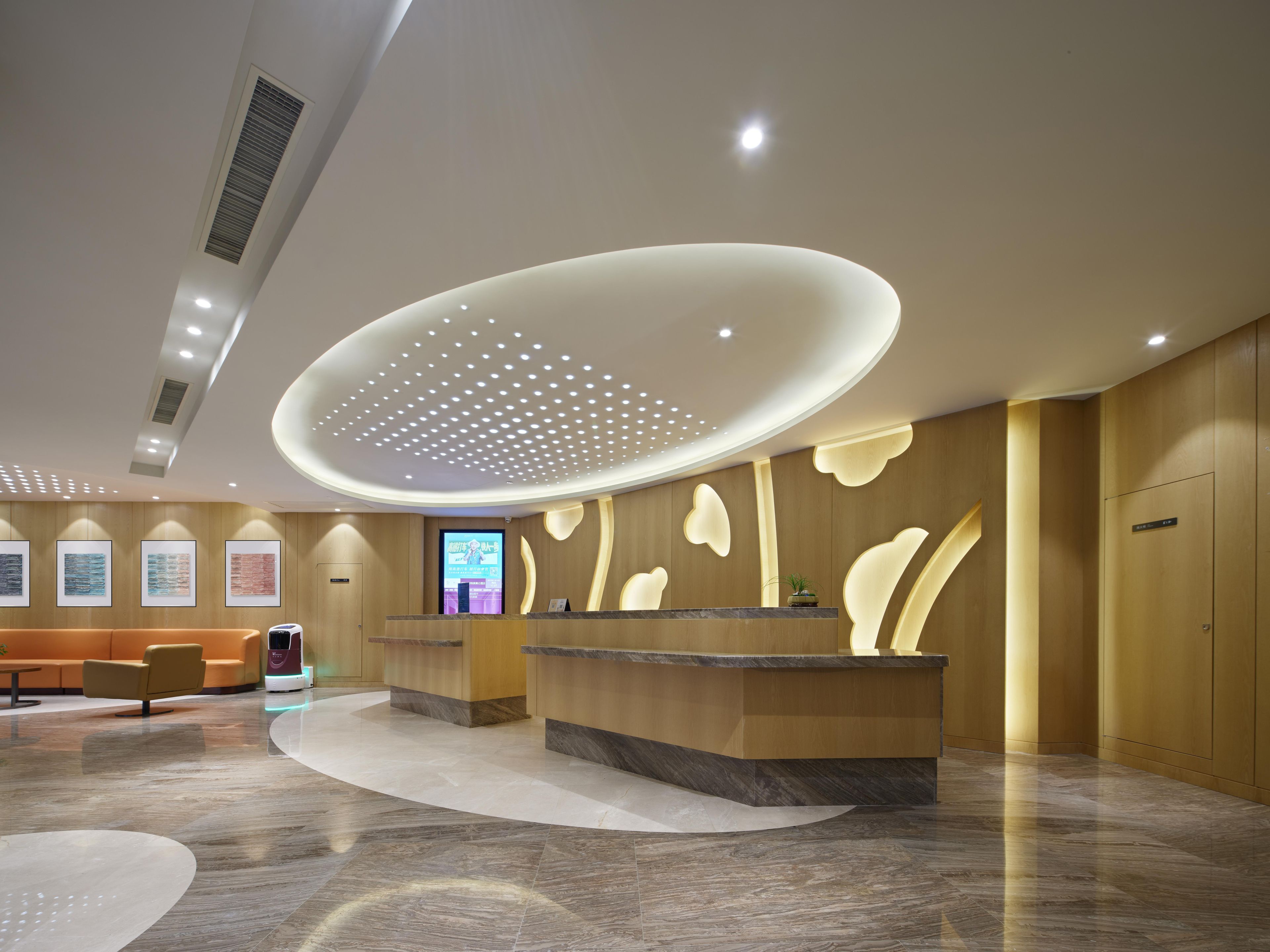 Un área de recepción moderna con un mostrador curvo, una pantalla digital y un espacio de espera con sofá y sillones.