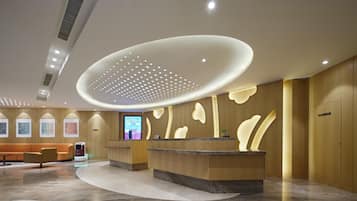 Un área de recepción moderna con un mostrador curvo, una pantalla digital y un espacio de espera con sofá y sillones.