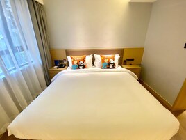 Una habitación de hotel con una cama grande, dos mesitas de noche y una ventana con cortinas.