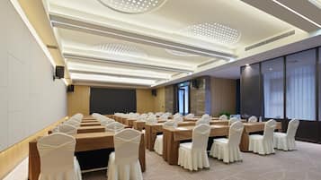 Un salón de conferencias con filas de mesas y sillas, una pantalla grande y un diseño moderno de techo.